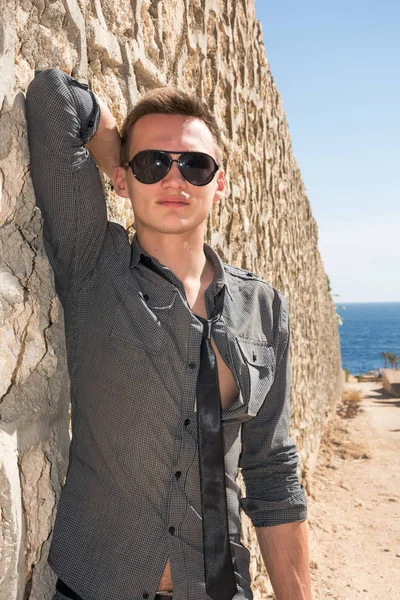 Hombre con gafas de sol de pie cerca de la pared en el camino hacia el mar — Foto de Stock