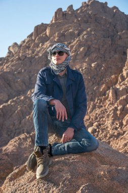 Çölde bir kayanın üzerine oturmuş bir keffiyeh adam