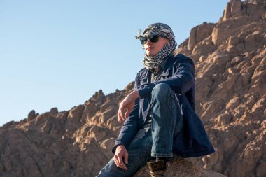 Çölde bir kayanın üzerine oturmuş bir keffiyeh adam