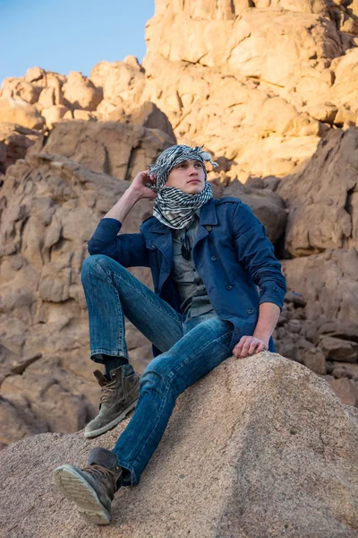 L'uomo in un keffiyeh seduto su una roccia nel deserto — Foto Stock