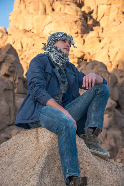 Man in a keffiyeh sitting on a rock in the desert — Stock Photo, Image