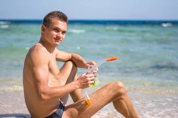 A young man sitting on the beach with a mask for diving, snorkel — Stock Photo, Image