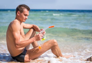 Dalış için bir maske ile sahilde oturan bir genç adam şnorkel