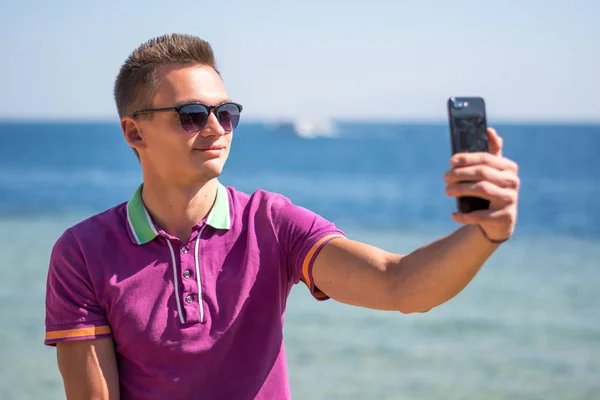 Homme en lunettes de soleil est assis avec un smartphone dans les mains près de la s — Photo