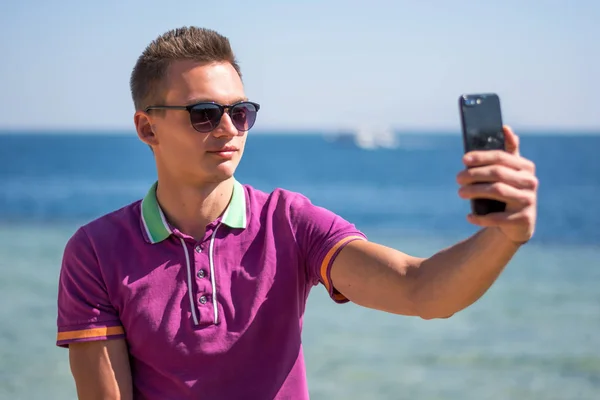 Man in sunglasses sits with a smartphone in the hands near the s — Stock Photo, Image