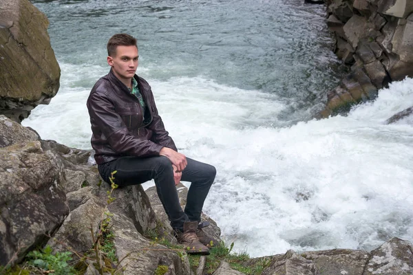 Young man sits near the waterfall — Stock Photo, Image
