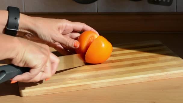 Female hand with a fitness bracelet cuts a yellow tomato on a cutting board — Stock Video