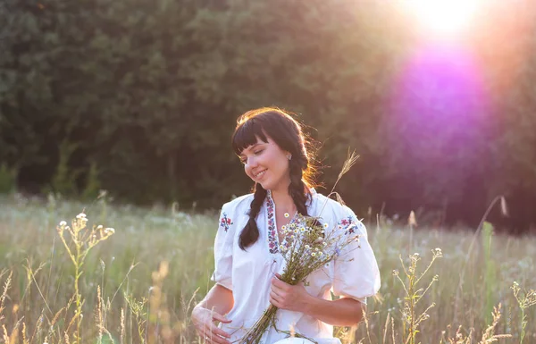 Uma jovem mulher em uma camisa bordada branca longa reúne flores — Fotografia de Stock