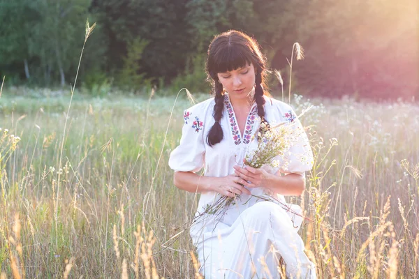 Kvinna i en lång vit broderad skjorta samlar blommor i en mea — Stockfoto