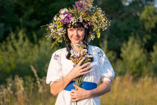 A young woman in a long white embroidered shirt and in a wreath 
