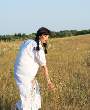 Uzun beyaz işlemeli tişört genç bir kadında çiçekler toplar 