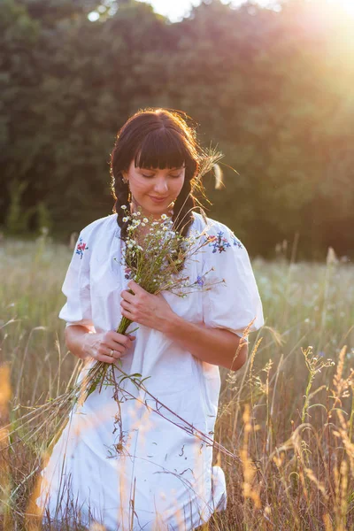 Mladá žena v dlouhé bílé vyšívané košile shromažďuje květiny — Stock fotografie