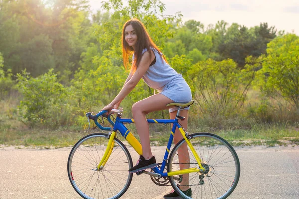 Young woman rides on a bicycle on the road in the park in the su — Stock Photo, Image