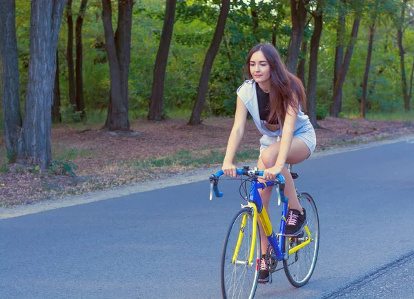 Young woman rides on a bicycle on the road in the park — Stock Photo, Image