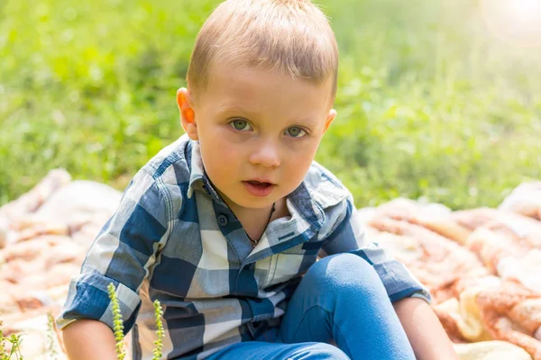 Un petit garçon est assis sur un plaid dans le parc — Photo