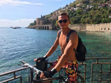 Genç bir adam bir sırt çantası ile deniz kenarında bisikletle seyahat eder. Görünüm 