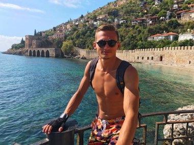 Genç bir adam bir sırt çantası ile deniz kenarında bisikletle seyahat eder. Seasc