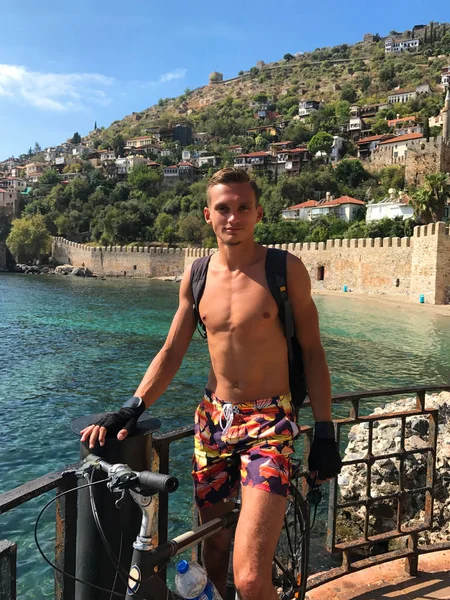 Genç bir adam bir sırt çantası ile deniz kenarında bisikletle seyahat eder. Görünüm 