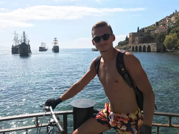 Genç bir adam bir sırt çantası ile deniz kenarında bisikletle seyahat eder. Görünüm 