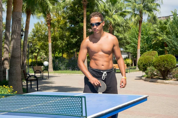 A young man plays table tennis without shirts in a park on a bac — Stock Photo, Image