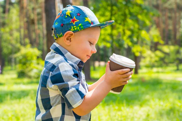 Petit garçon tenant un verre en plastique avec du thé dans le parc sur un soleil — Photo