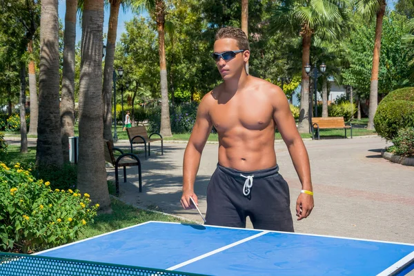 A young guy plays table tennis without shirts in a park on a bac — Stock Photo, Image