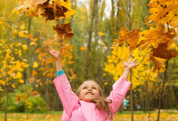 Девушка в плаще осенью бросает желтые листья в парке . — стоковое фото