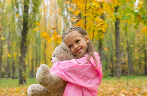 Маленькая девочка в розовом плаще обнимает плюшевого медведя в... — стоковое фото