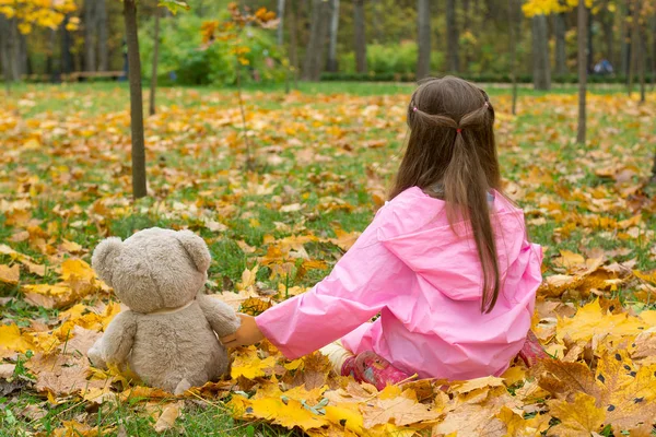 Маленькая девочка в розовом плаще держит плюшевого медведя за лапой — стоковое фото