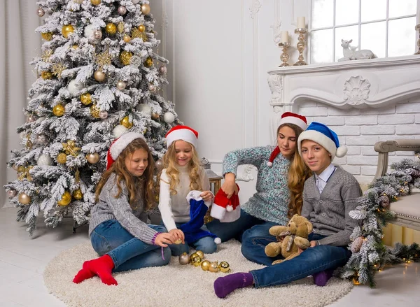 Children in Santa caps are decorate a Christmas tree in a room. — Stock Photo, Image