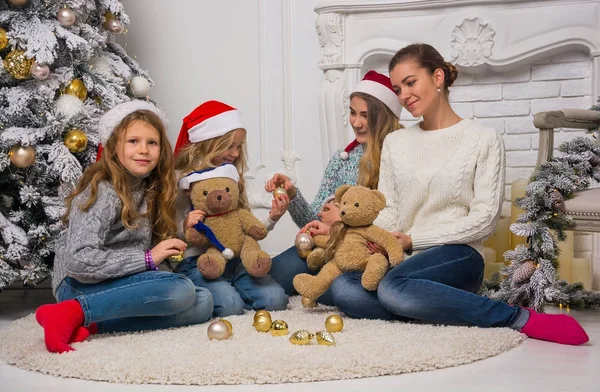 Niños y mamá con sombreros de Papá Noel sentados cerca de un árbol de Navidad —  Fotos de Stock