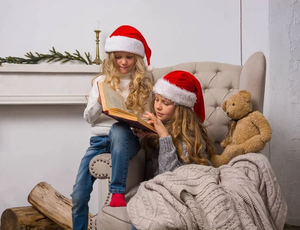 Zwei kleine Mädchen mit Weihnachtsmützen lesen ein Buch — Stockfoto