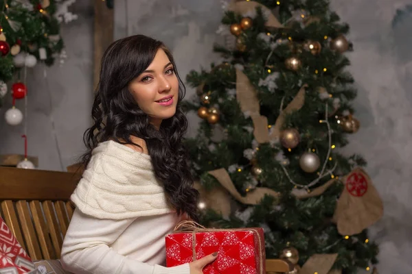 A young woman holds a gift near the Christmas tree. — Stock Photo, Image