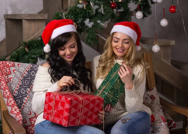 Two beautiful women in santa hats smiles unfold gifts for Christ — Stock Photo, Image