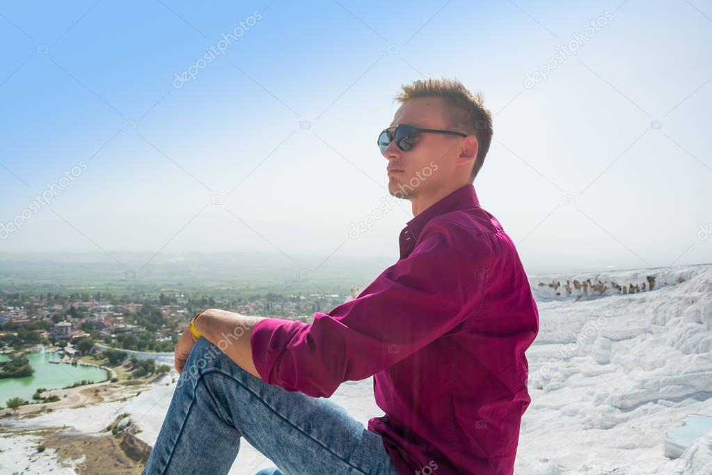 Young guy in sunglasses sits and admires the view of Pamukkale, 