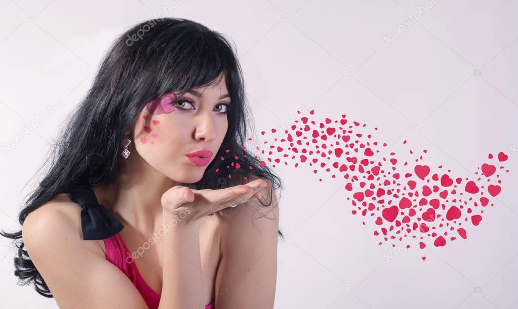 A beautiful woman with a heart on her cheek blows on her hand an