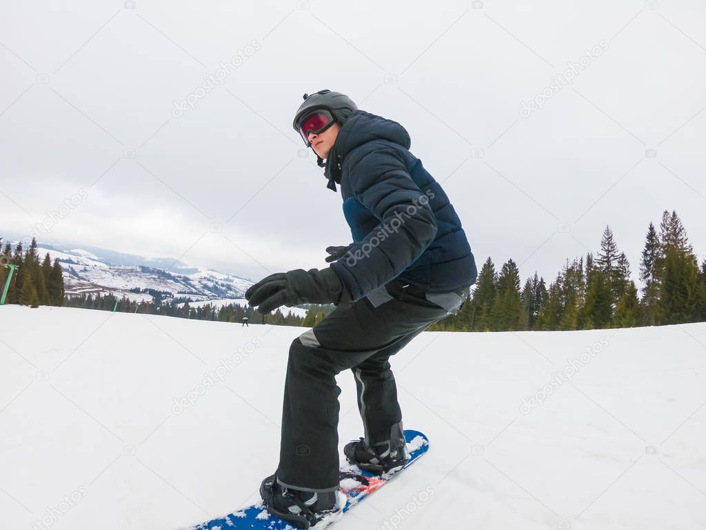 A young man in sports glasses is riding a snowboard in the mount