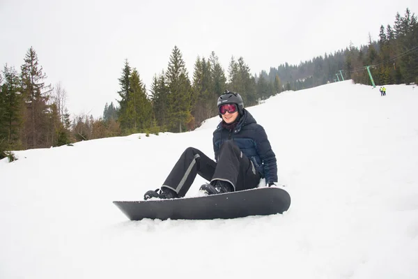 Een jonge man in een helm en sportbril valt, ik snowboarden — Stockfoto