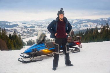 Bir kask ile bir kar arabası yakınındaki bir eylem fotoğraf makinesi içinde genç bir adam 