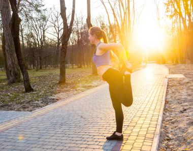 Genç kadın parkta günbatımında çalıştırmadan önce ısıtır. 