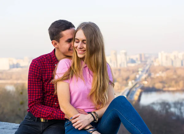 Um cara abraça uma garota contra o pano de fundo de uma paisagem urbana na primavera — Fotografia de Stock