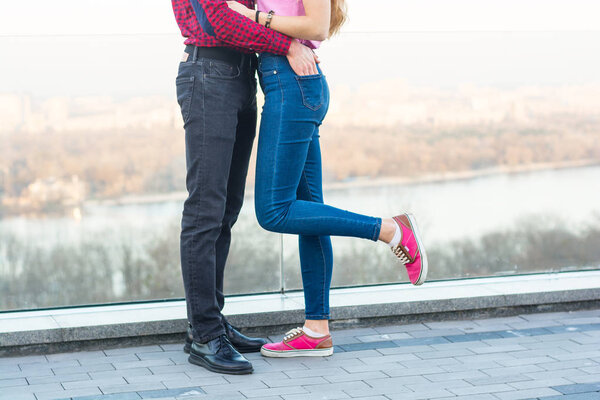 The legs of a guy and a girl who embrace on the background of the cityscape
