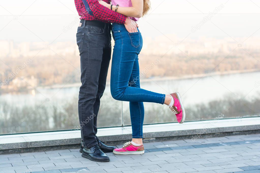 The legs of a guy and a girl who embrace on the background of the cityscape