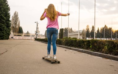 Genç bir kadın yaz aylarında bir parkta bir kaykay sürme