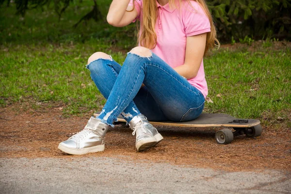 Legs of a girl who is sitting on a skateboard — Stock Photo, Image