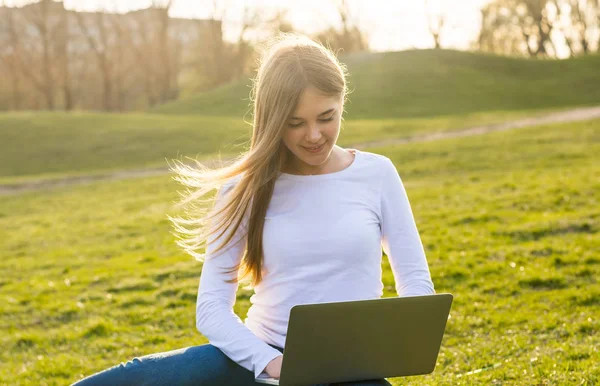 Joven hermosa chica-estudiante con un ordenador portátil sentado en la hierba en s —  Fotos de Stock