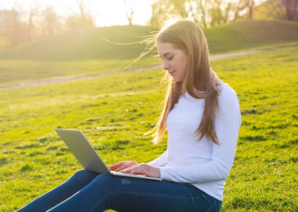 Joven hermosa mujer con un ordenador portátil sentado en la hierba en verano —  Fotos de Stock