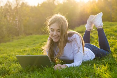 Genç güzel kız öğrenci bir dizüstü bilgisayar ile çim üzerinde yalan 