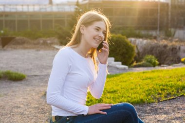 Genç güzel kadın bahar gün batımında cep telefonuyla konuşuyor