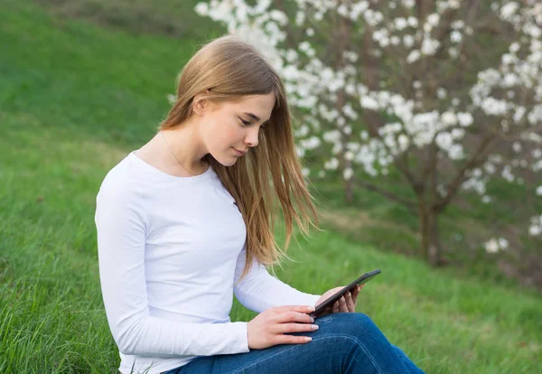 Joven hermosa chica se sienta con una tableta en un gar primavera floreciente —  Fotos de Stock